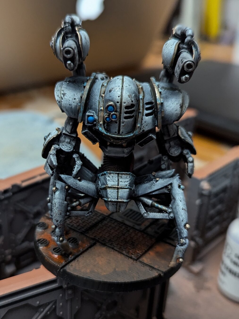 A painted Warhammer 40k mini. A crab-like robot with white armor plates standing on a rusty base.