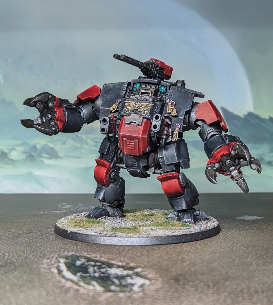 A photograph of a painted Warhammer 40,000 miniature. A dreadnaught with two claws, a pair of flame thrower, and black armor with red and gold accents.