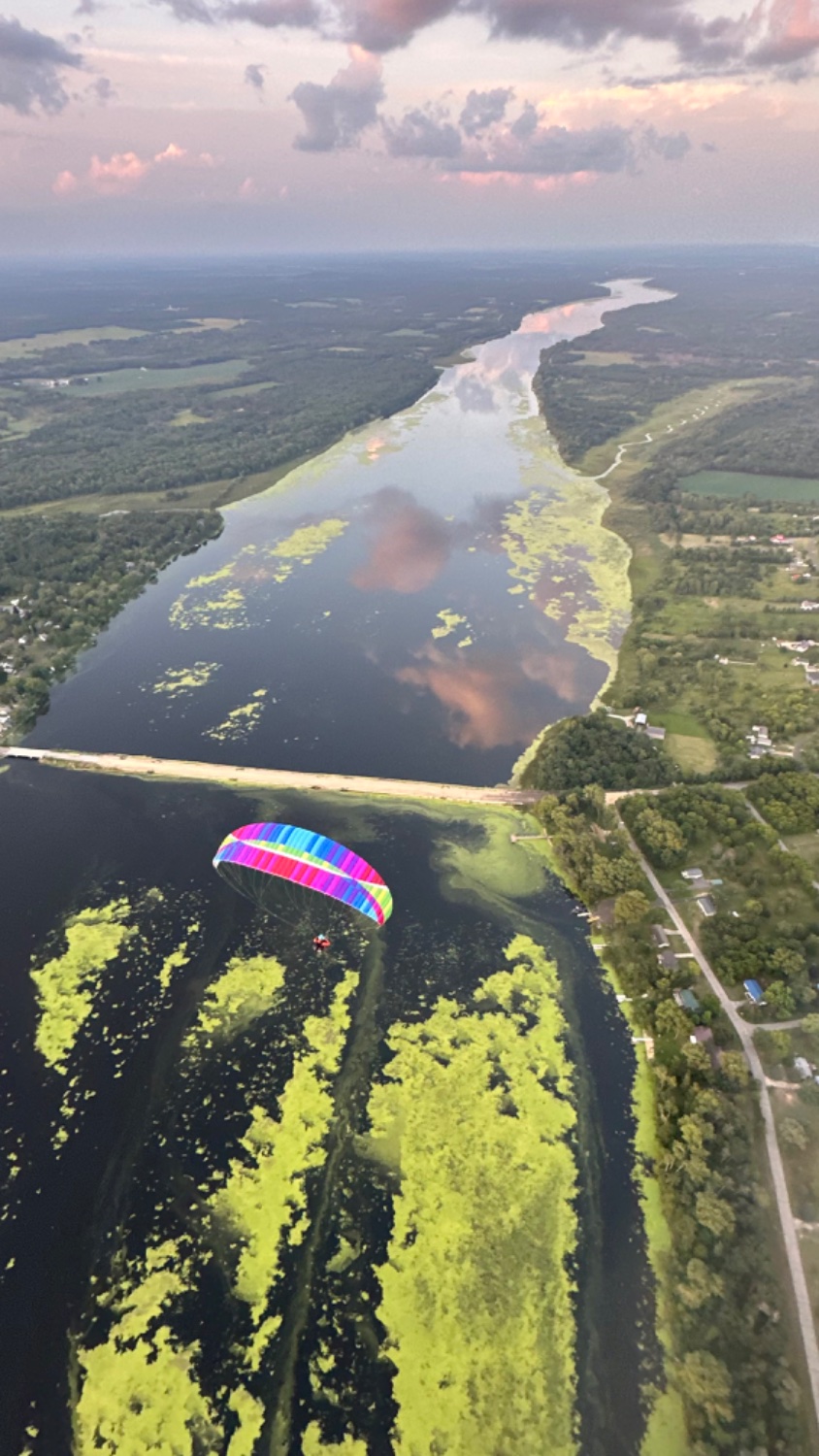 Flying a Paramotor over a wide river in Wisconsin. The river is covered with green algae and there is a road crossing it.