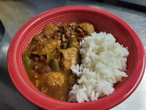 red bowl half filled with white rice and half filled with a stew of beans and what appears to be chunks of sausage and bell pepper