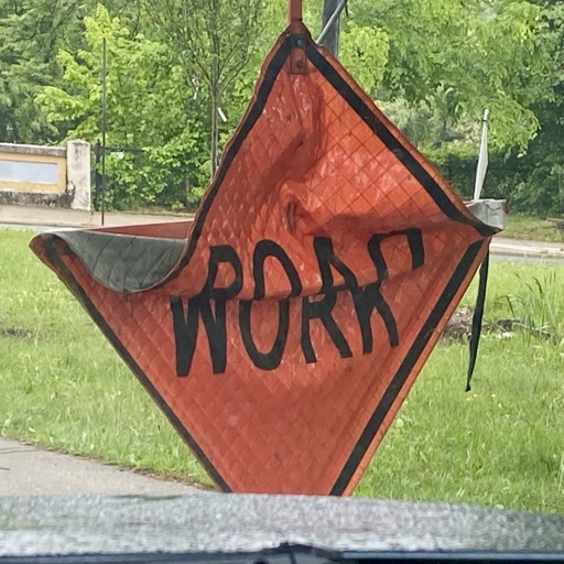 A “ROAD WORK” sign partially folded in the middle, blending the top of the word “ROAD” and the bottom of the word “WORK” into a combination that resembles the word “ROAR.”